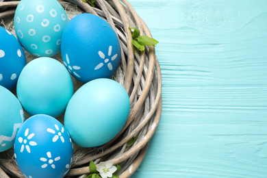 Nest with Easter eggs on light blue wooden background, top view. Space for text