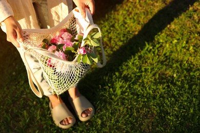 Photo of Woman holding mesh bag with beautiful tea roses outdoors, above view. Space for text