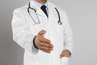 Male doctor offering handshake on light grey background, closeup