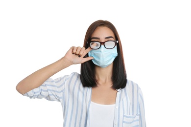 Young woman wiping foggy glasses caused by wearing disposable mask on white background. Protective measure during coronavirus pandemic