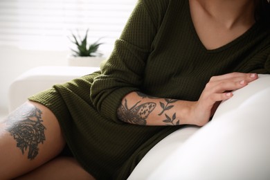 Beautiful woman with tattoos on body resting in living room, closeup