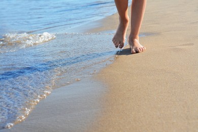 Child walking through water on seashore, closeup of legs. Space for text
