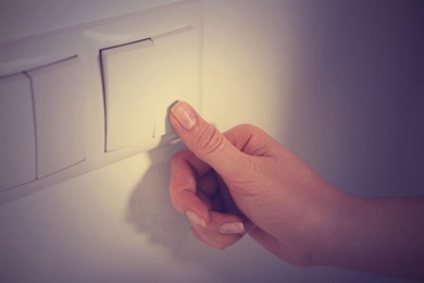 Photo of Woman turning off light switch indoors, closeup. Energy saving concept