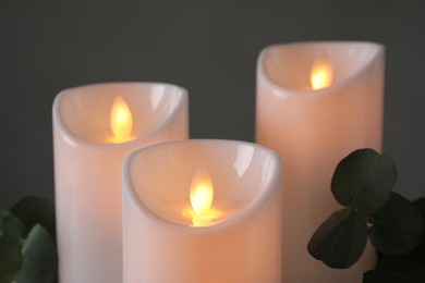 Decorative LED candles and eucalyptus on grey background, closeup