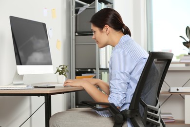 Photo of Young woman with bad posture sitting at workplace in office. Symptom of scoliosis
