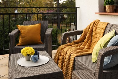 Photo of Colorful pillows, soft blanket and yellow chrysanthemum flowers on rattan garden furniture outdoors