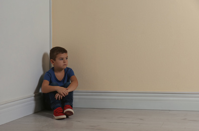 Little boy sitting in corner near yellow wall, space for text. Child in danger