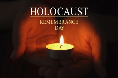 Image of International Holocaust Remembrance Day. Woman holding burning candle in darkness, closeup