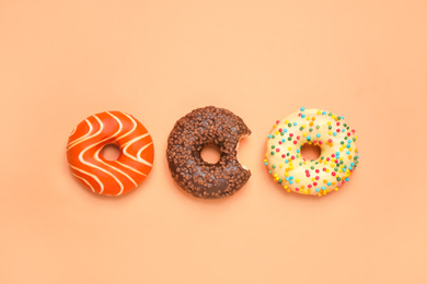 Delicious glazed donuts on orange background, flat lay