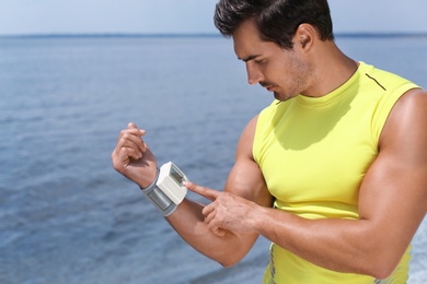 Photo of Young man checking pulse with medical device after training on beach