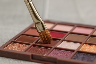 Photo of Colorful eyeshadow palette with brush on grey table, closeup view