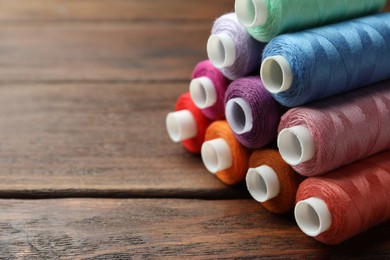 Photo of Stack of colorful sewing threads on wooden table, closeup. Space for text