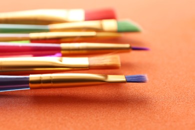 Set of different paintbrushes on orange background, closeup
