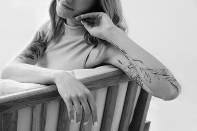 Beautiful woman with tattoos on arms resting indoors, closeup. Black and white photography