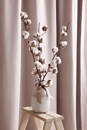 Vase with beautiful bouquet of white fluffy cotton flowers on wooden decor ladder