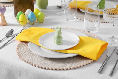 Photo of Festive table setting with cutlery, plate and bunny figure. Easter celebration