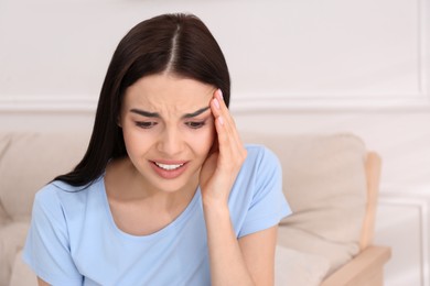 Young woman suffering from migraine at home, space for text
