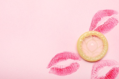 Condom with lipstick kiss marks and space for text on pink background, top view. Safe sex