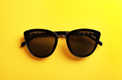 Stylish sunglasses on yellow background, top view