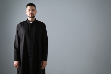 Priest wearing cassock with clerical collar on grey background, space for text
