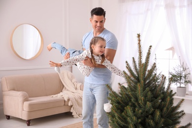 Father with his cute daughter having fun near fir tree at home. Christmas atmosphere