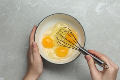 Woman whisking eggs in bowl at light grey table, top view