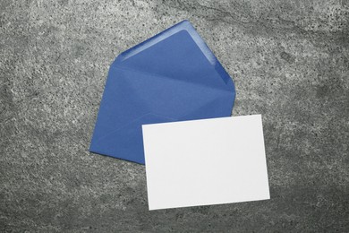 Envelope with blank paper card on grey table, top view