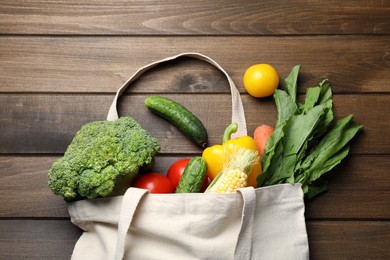 Cloth bag with different vegetables on wooden table, flat lay