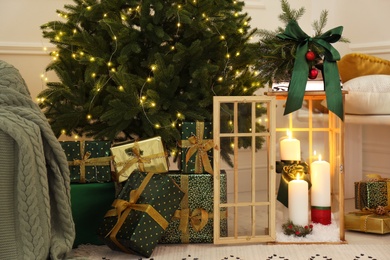 Wooden decorative lantern with burning candles near Christmas tree in room