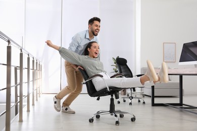 Office employee giving his colleague ride in chair at workplace