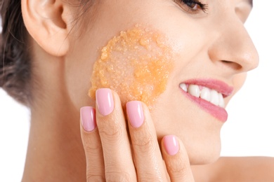 Young woman applying natural scrub on her face against white background, closeup