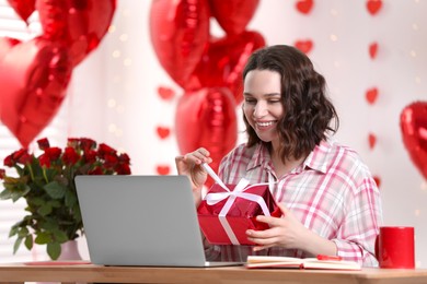Photo of Valentine's day celebration in long distance relationship. Woman opening gift from her boyfriend indoors