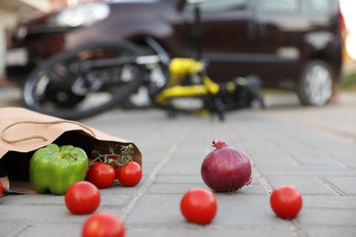 Fallen bicycle after car accident outdoors, focus on scattered vegetables