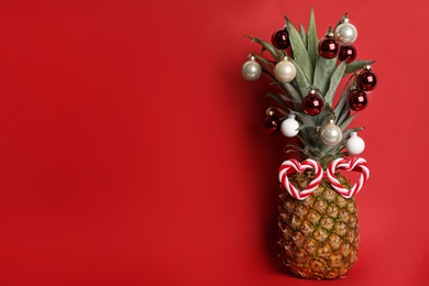 Pineapple with party glasses and Christmas tree balls on red background, space for text. Creative concept