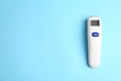 Modern non-contact infrared thermometer on light blue background, top view. Space for text