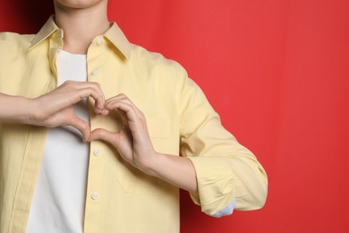 Photo of Woman making heart with hands on red background, closeup. Space for text