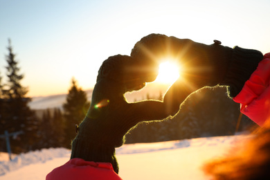 Woman making heart with hands outdoors at sunset, closeup. Winter vacation