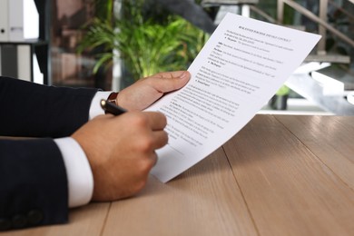 Man signing Real Estate Purchase And Sale Contract at wooden table indoors, closeup