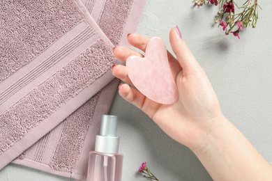 Photo of Woman with rose quartz gua sha tool at white table, top view