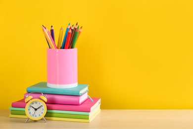 Different school stationery and alarm clock on table against yellow background, space for text. Back to school