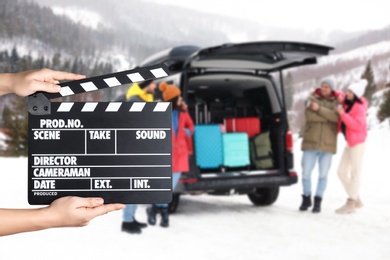Assistant holding clapperboard and people near car on snowy road, closeup. Cinema production 
