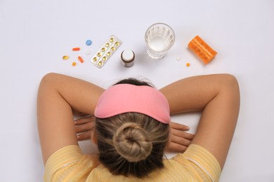 Woman surrounded by different pills on white background, top view. Insomnia treatment