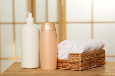 Soft folded terry towels in wicker basket and cosmetic bottles on wooden table indoors