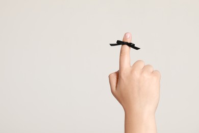 Man showing index finger with black tied bow as reminder on white background, closeup. Space for text