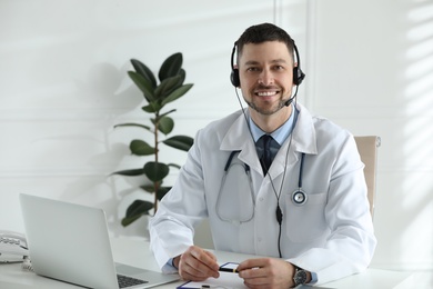 Doctor with headset sitting at desk in clinic. Health service hotline