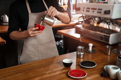 Barista pouring milk into cup of coffee in shop, closeup