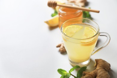 Photo of Glass of aromatic ginger tea and ingredients on light grey background, space for text