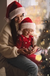 Mother and daughter in Santa hats playing with snow globe near window