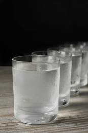 Shot glasses of cold vodka on wooden table against grey background, closeup