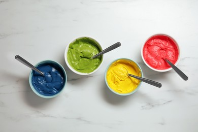 Photo of Bowls of different cream with food coloring on white marble table, flat lay